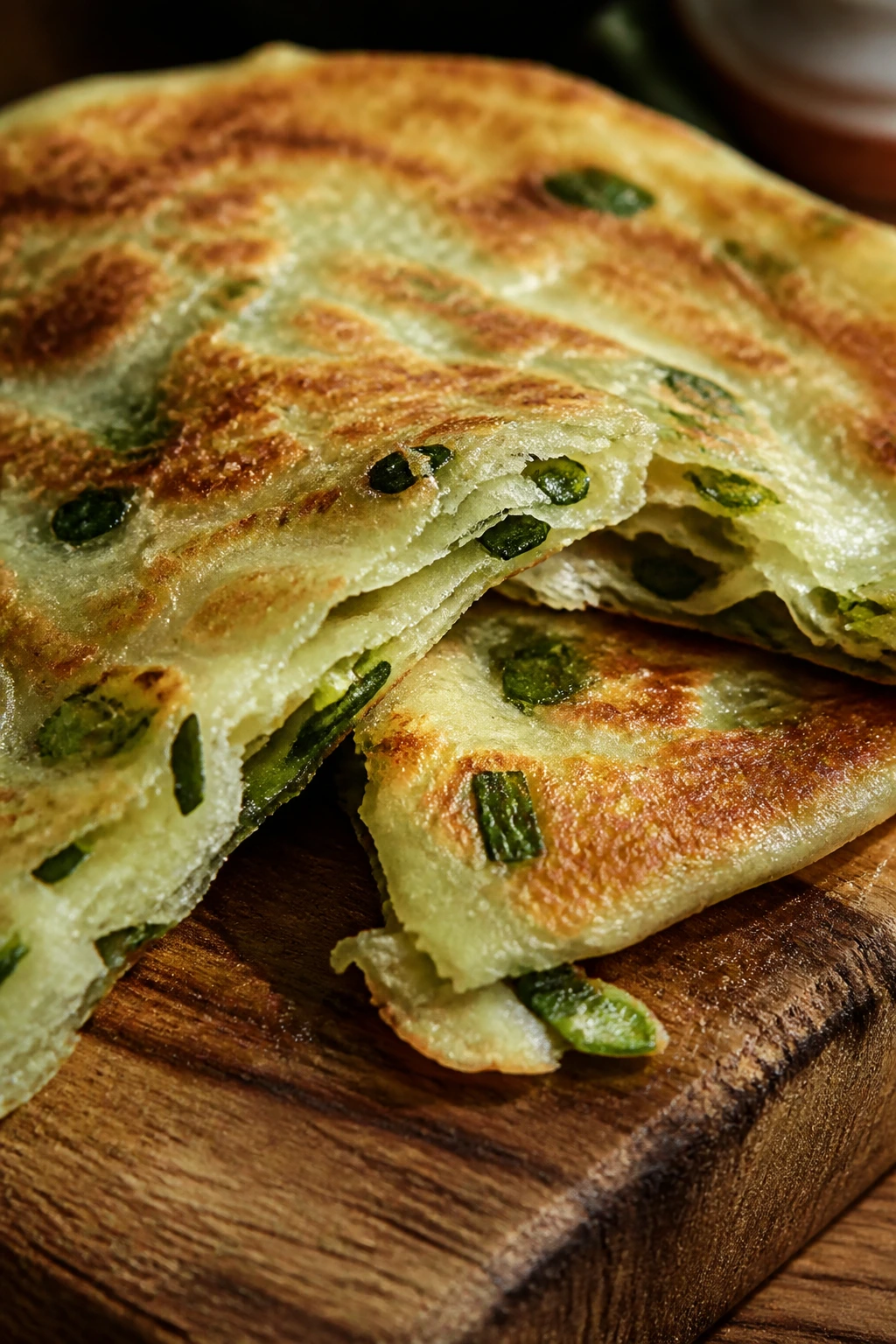 Close-up of a flaky scallion pancake showing layered interior on a wooden board