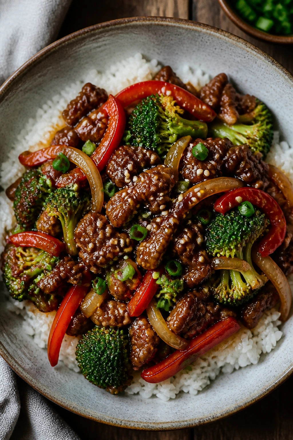 Top-down sesame beef bowl with broccoli, peppers, and onions