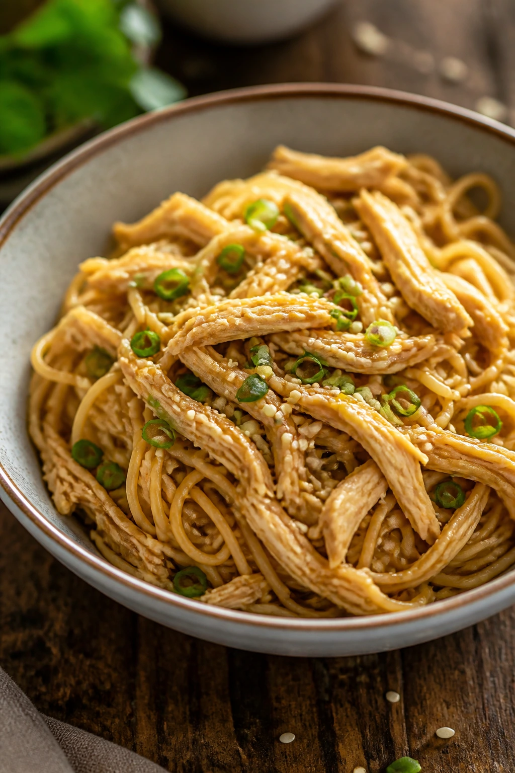 Medium close-up of sesame noodles with chicken in a glossy sauce