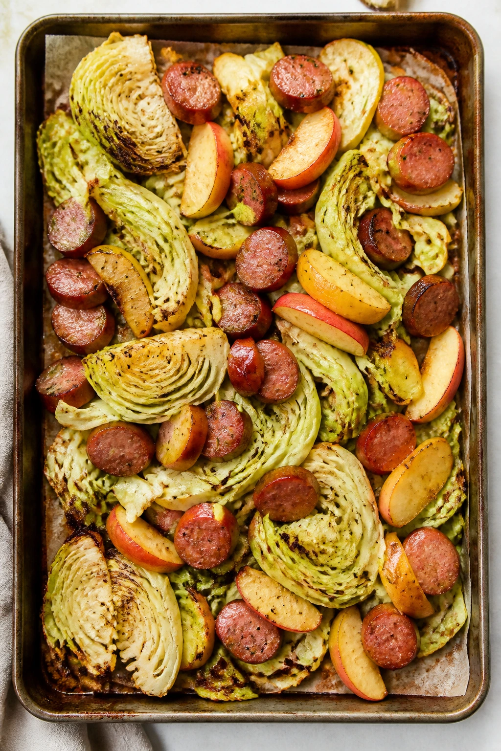 Top-down view of roasted smoked sausage with apples and cabbage on a sheet pan.
