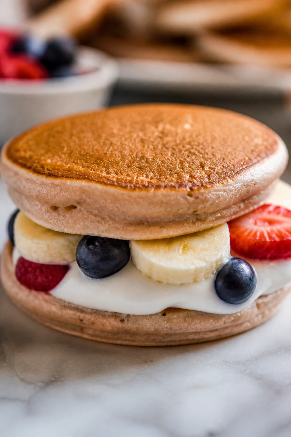 Close-up of a smoothie pancake sandwich with yogurt and fruit filling on a plate in a warm kitchen