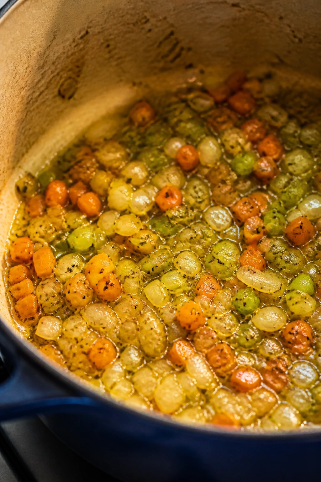 Soffritto base simmering in olive oil inside a rustic Dutch oven