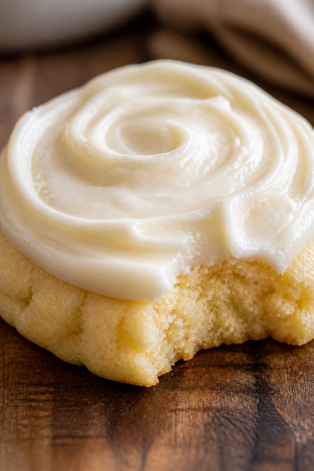 Close-up of a plush soft cookie with cream cheese frosting on a wooden counter