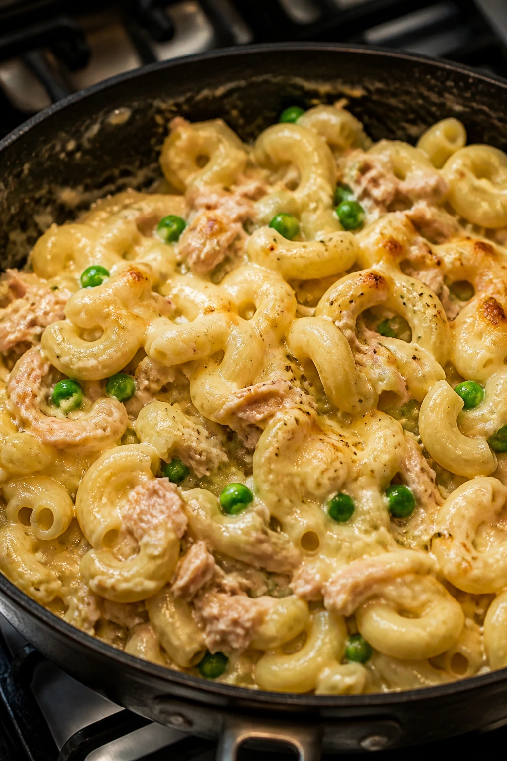 Creamy tuna pasta with peas and melted cheese in a skillet