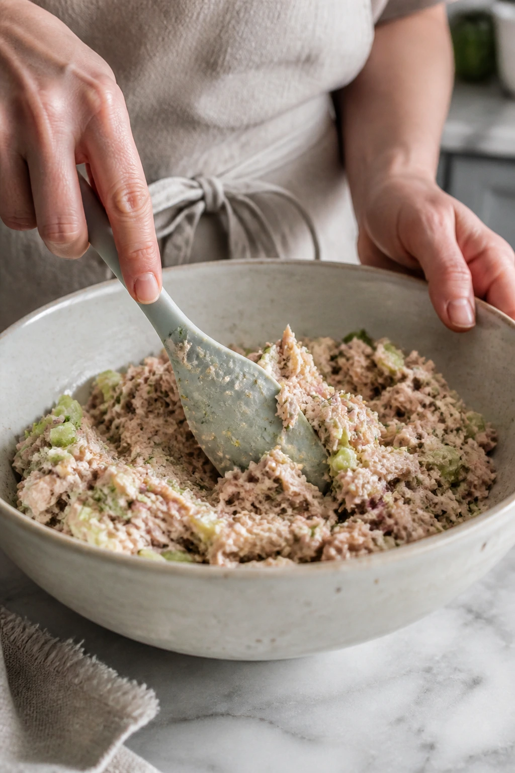 Hands gently folding tuna salad to keep tuna flakes intact