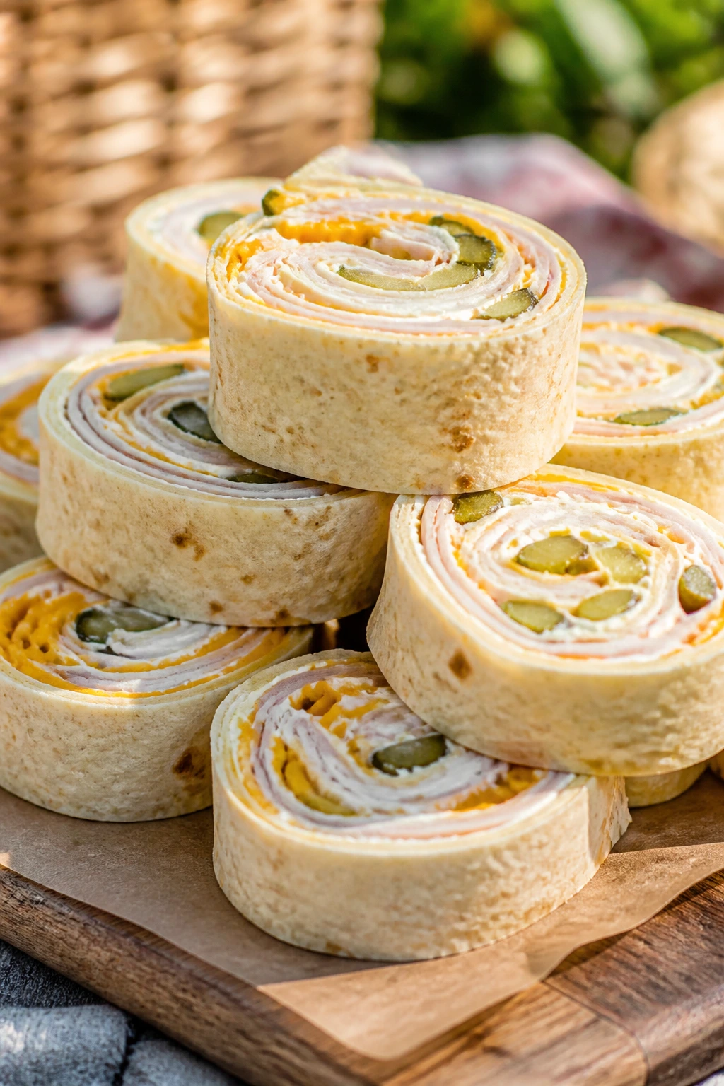 Close-up of turkey cheddar pickle wraps sliced in half on a wooden board outdoors.