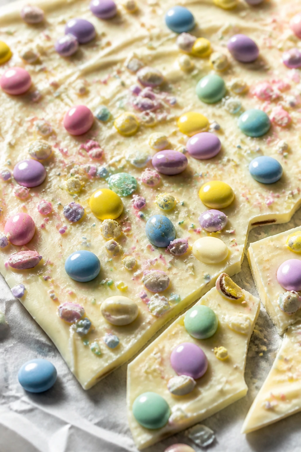 Close-up of white chocolate bark with pastel toppings on parchment.